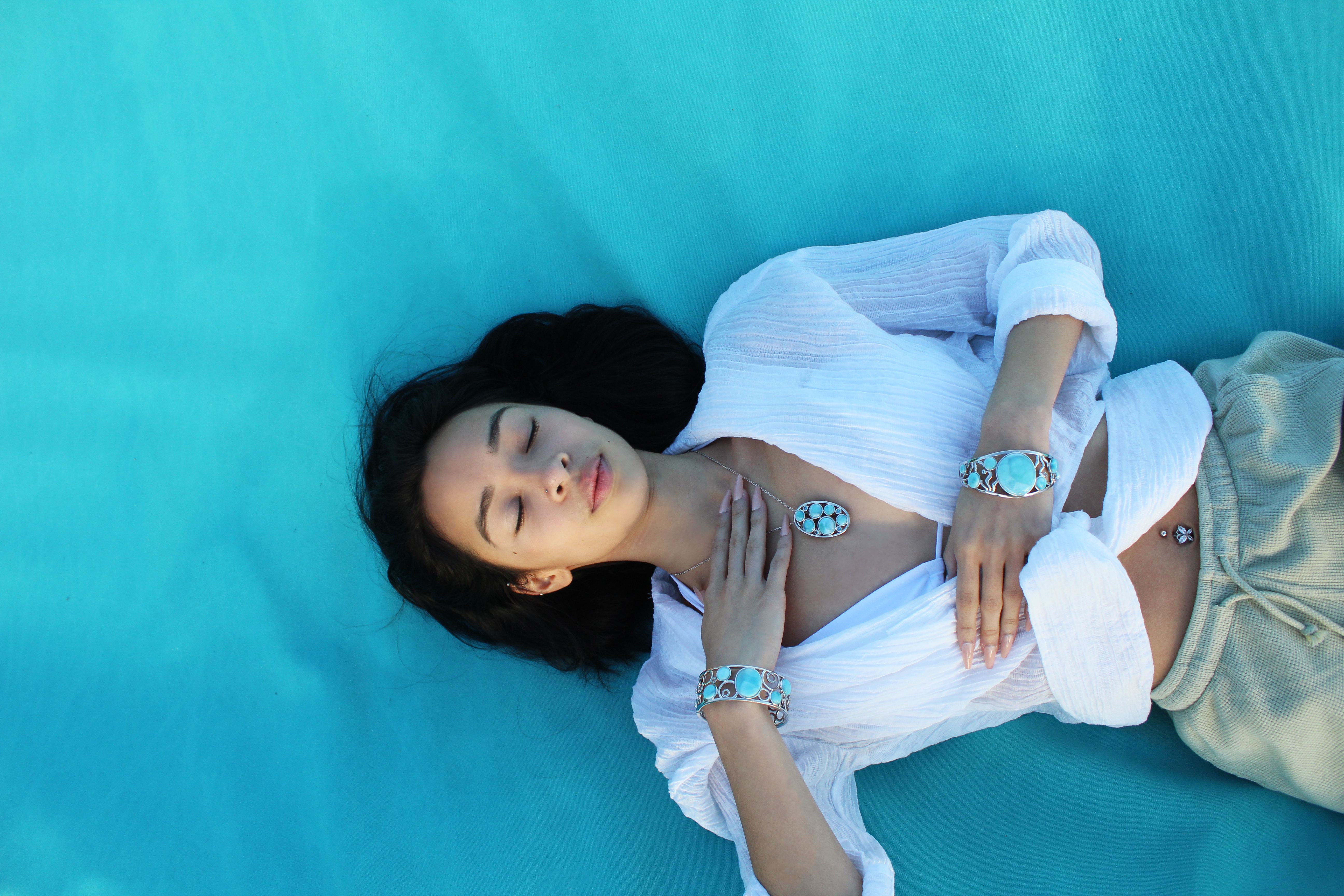the photo shows a woman laying down with a blue background and Larimar jewelry. 