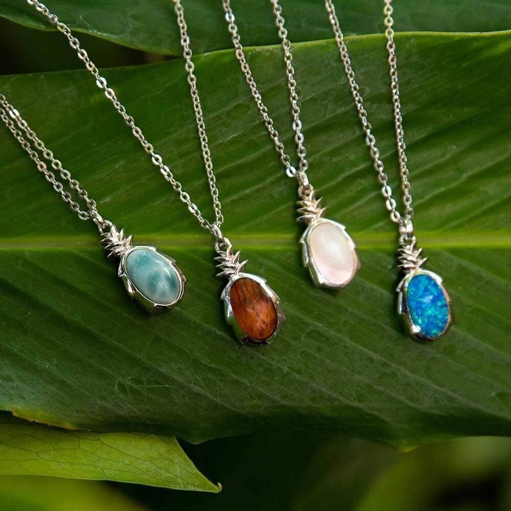 four pineapple pendants with different gemstones. From left to right, we have larimar, koa wood, mother of pearl and our sustainable ocean blue opalite
