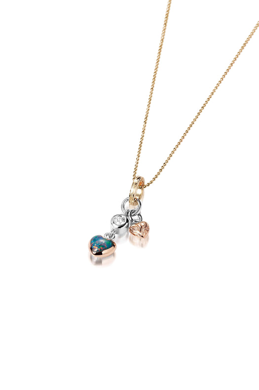The picture shows a 14K yellow, white, and rose gold opal two-heart charm pendant with hand engravings and a diamond.