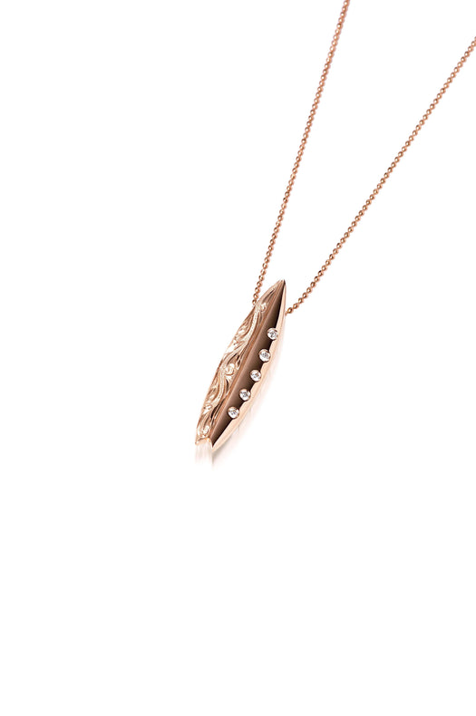 In this photo there is a rose gold surfboard pendant with diamonds and hand engravings.