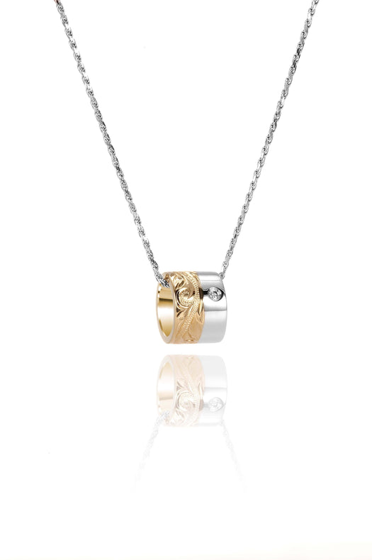 This picture shows a 14k yellow and white gold two-tone barrel pendant with hand engravings and a diamond.