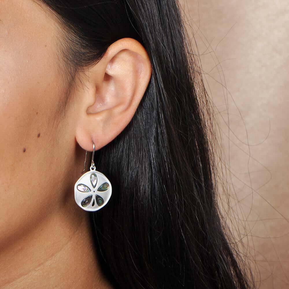Sterling silver abalone earrings with a sand dollar design worn by a model. 