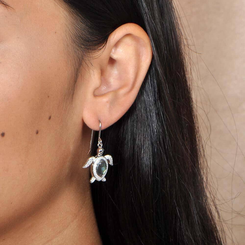 Sterling silver, abalone, and pave sea turtle hook earring worn by a model.