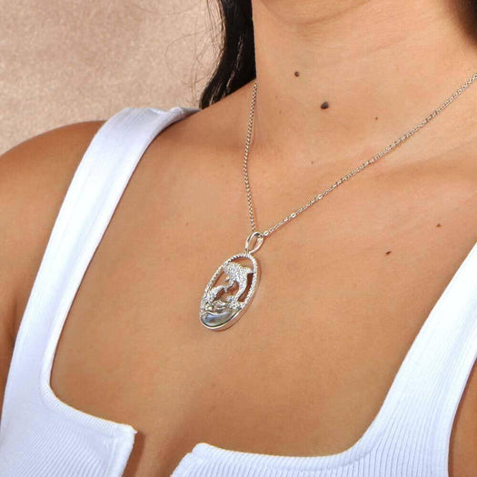 Sterling Silver, white topaz, and abole pendant designed like two dolphins. The pendant is worn by a model. 