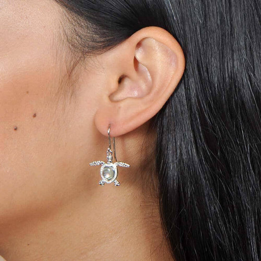 Sterling silver sea turtle hook earrings featuring Pave detail and an abalone shell. Worn by a model.