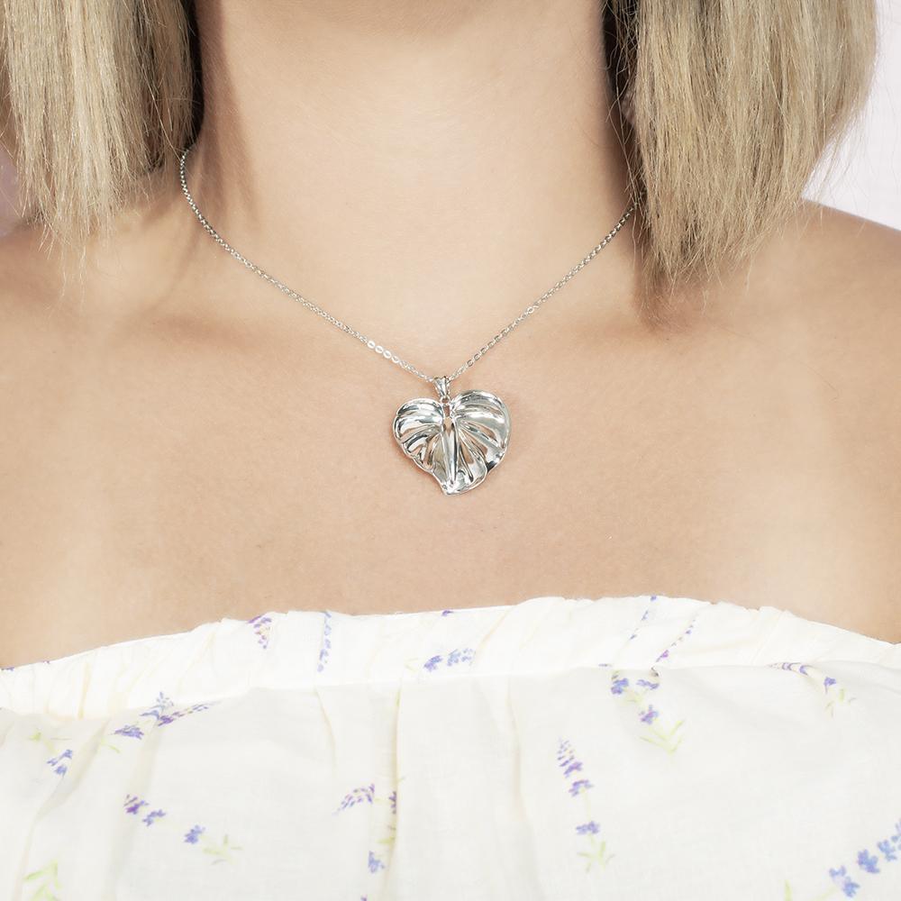 In this photo there is a model with blonde hair and a white shirt with purple flowers, wearing a  sterling silver anthurium pendant.