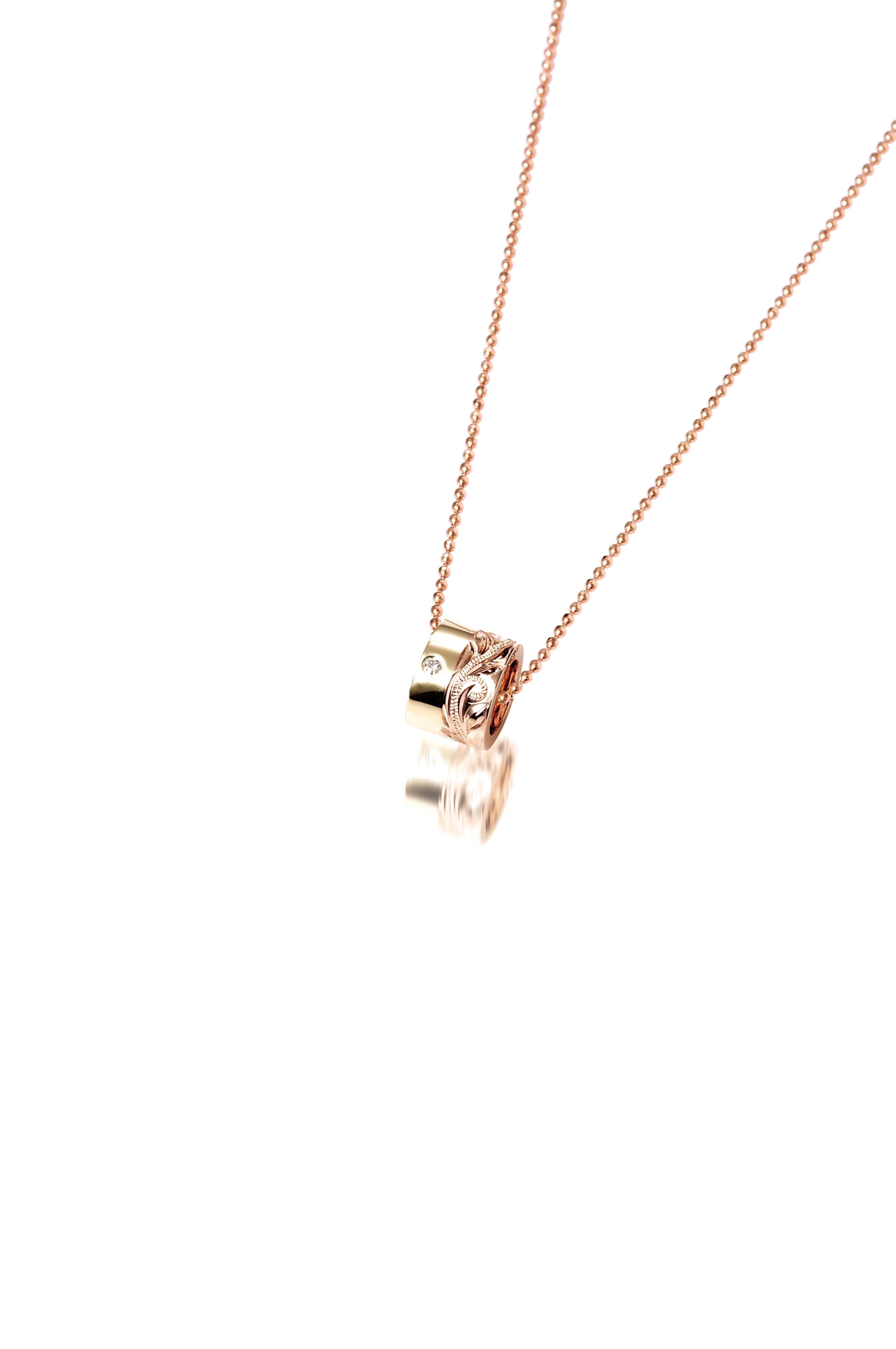This picture shows a 14k yellow and rose gold two-tone barrel pendant with hand engravings and a diamond.