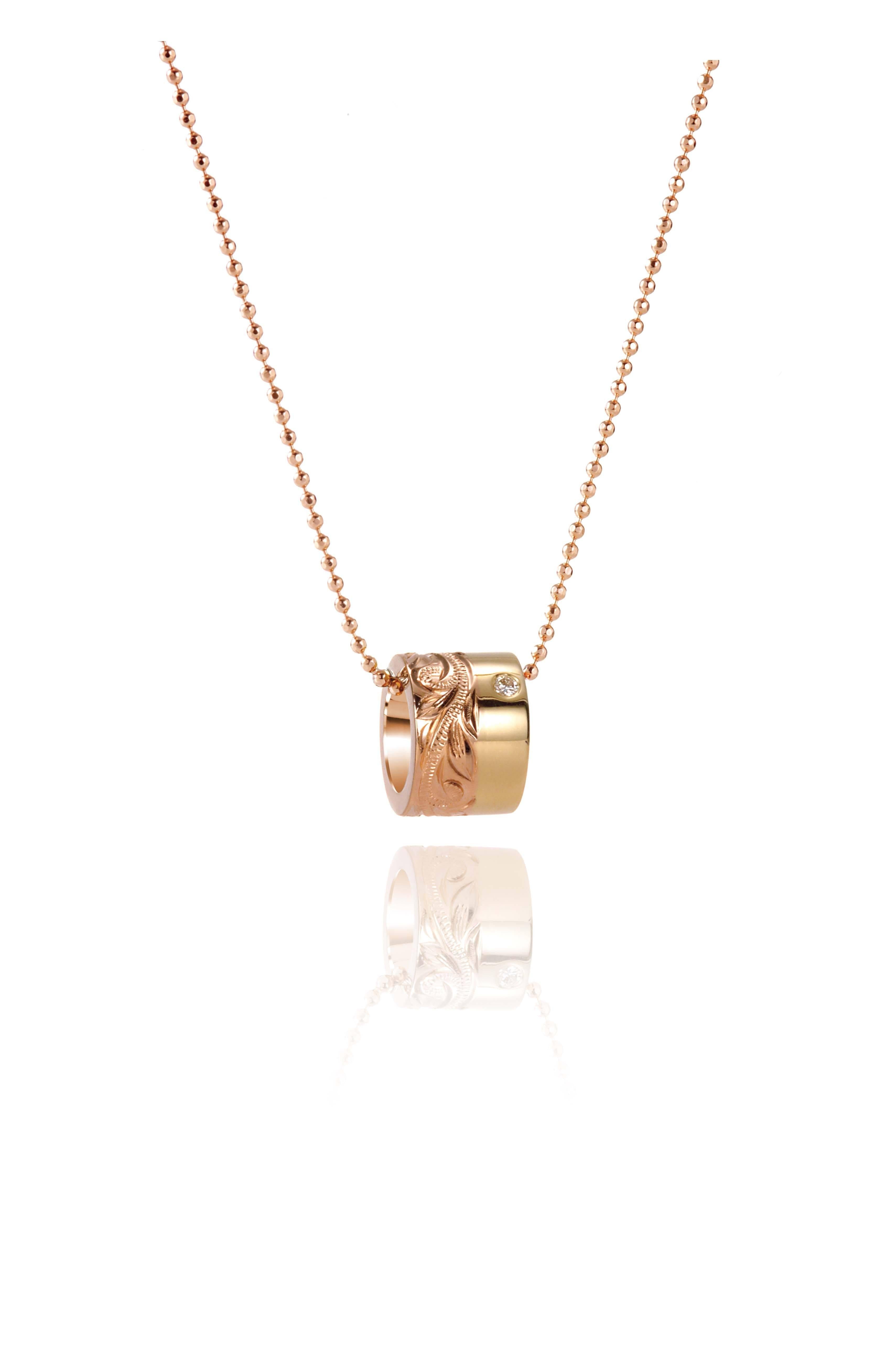 This picture shows a 14k yellow and rose gold two-tone barrel pendant with hand engravings and a diamond.