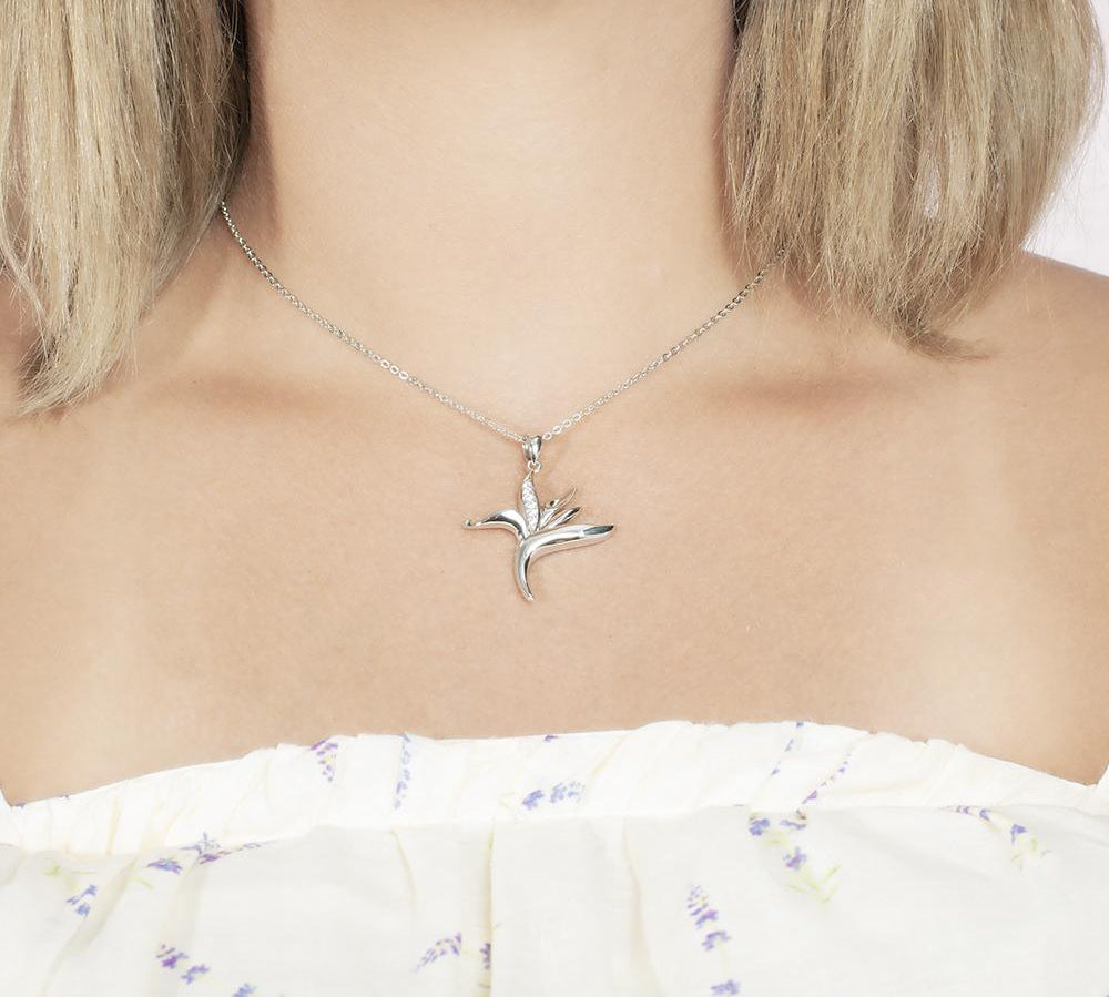 In this photo there is a model with blonde hair and a white shirt with purple flowers, wearing a sterling silver bird of paradise pendant with cubic zirconia.