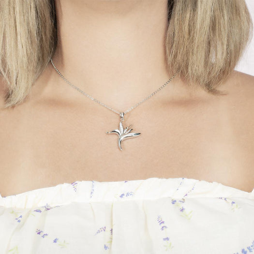 In this photo there is a model with blonde hair and a white shirt with purple flowers, wearing a sterling silver bird of paradise pendant with cubic zirconia.