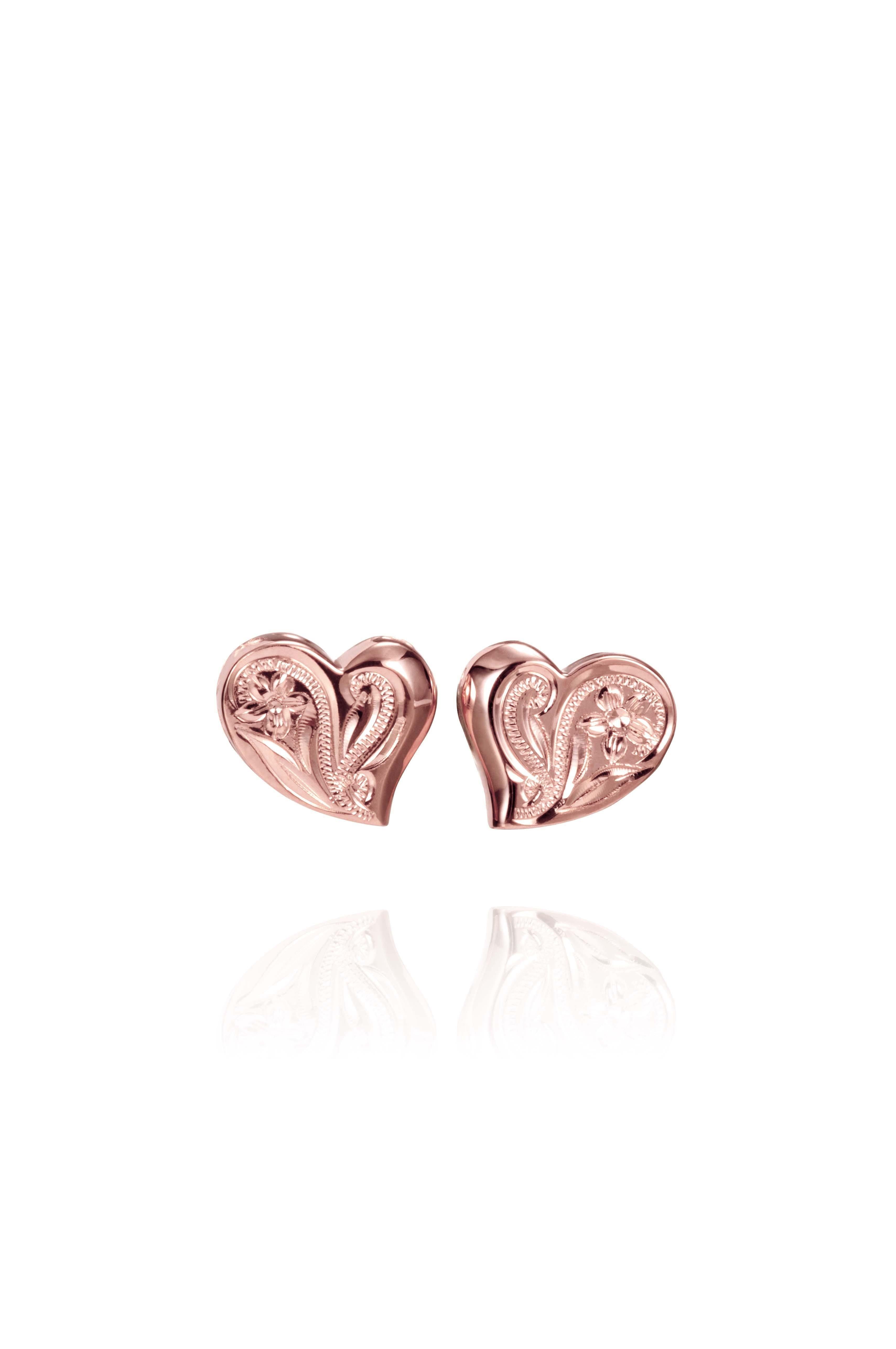 In this photo there is a pair of 14k rose gold heart stud earrings with plumeria flower engravings.