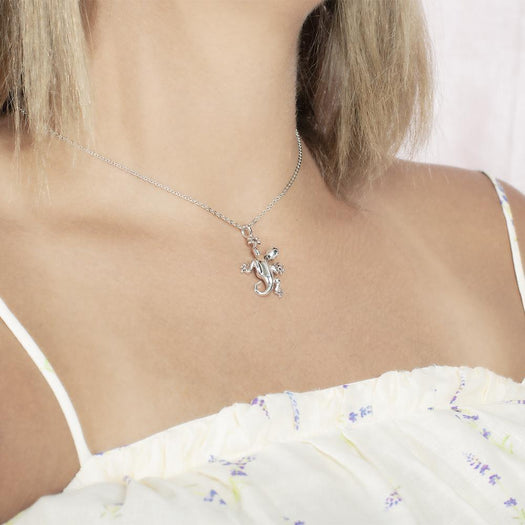 In this photo there is a model turned to the right with blonde hair and a white shirt with purple flowers, wearing a sterling silver gecko pendant.