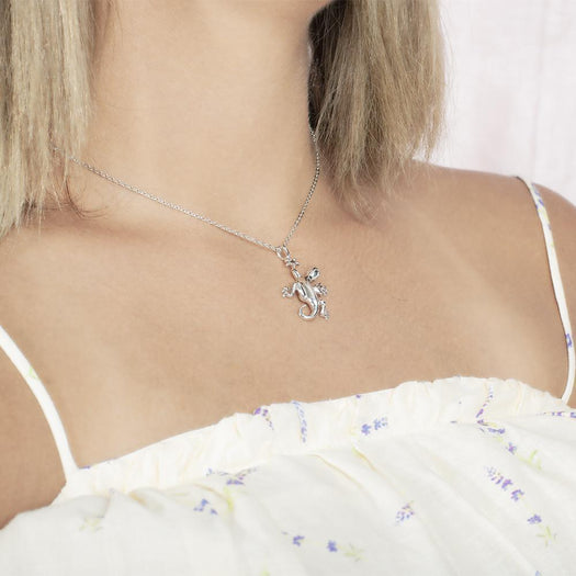 In this photo there is a model turned to the right with blonde hair and a white shirt with purple flowers, wearing a sterling silver gecko pendant.