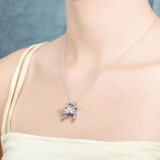The picture shows a model wearing a 925 sterling silver sea turtle pendant with hibiscus cut-out and cubic zirconia.