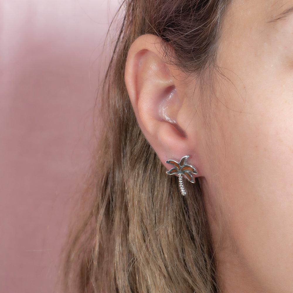 Pair of 925 sterling silver and koa wood palm tree stud earrings. The earrings are worn by a model.