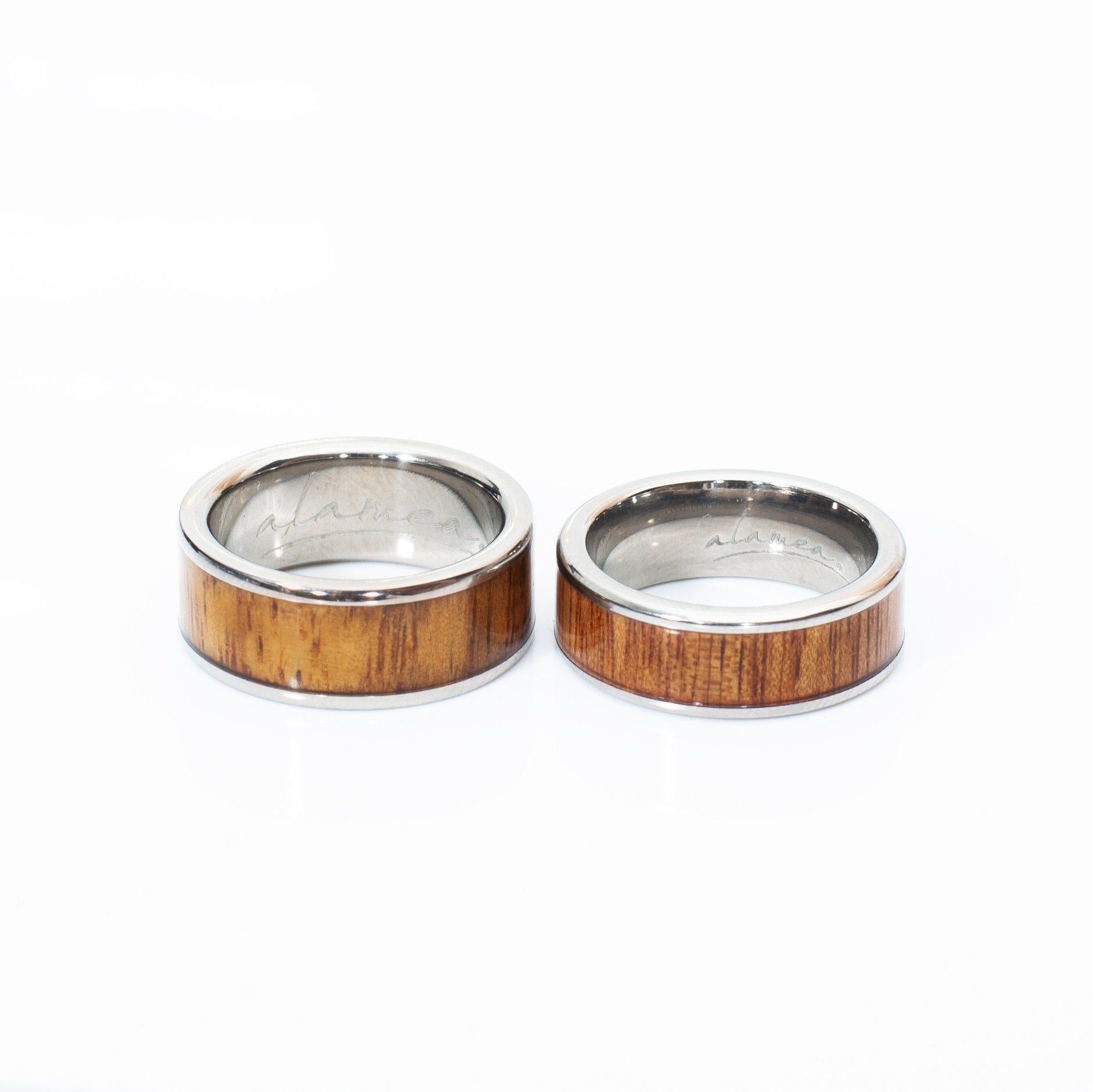 In this photo there are two rings made of koa wood and titanium placed side-by-side.