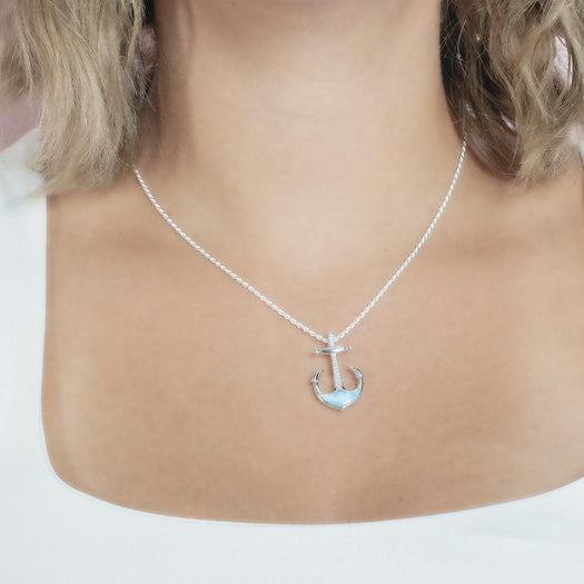 In this photo there is a model with blonde hair and a white shirt, wearing a sterling silver anchor pendant with blue larimar and topaz gemstones.