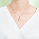 In this photo there is a model with a white shirt wearing a sterling silver fish hook pendant with blue larimar gemstones.