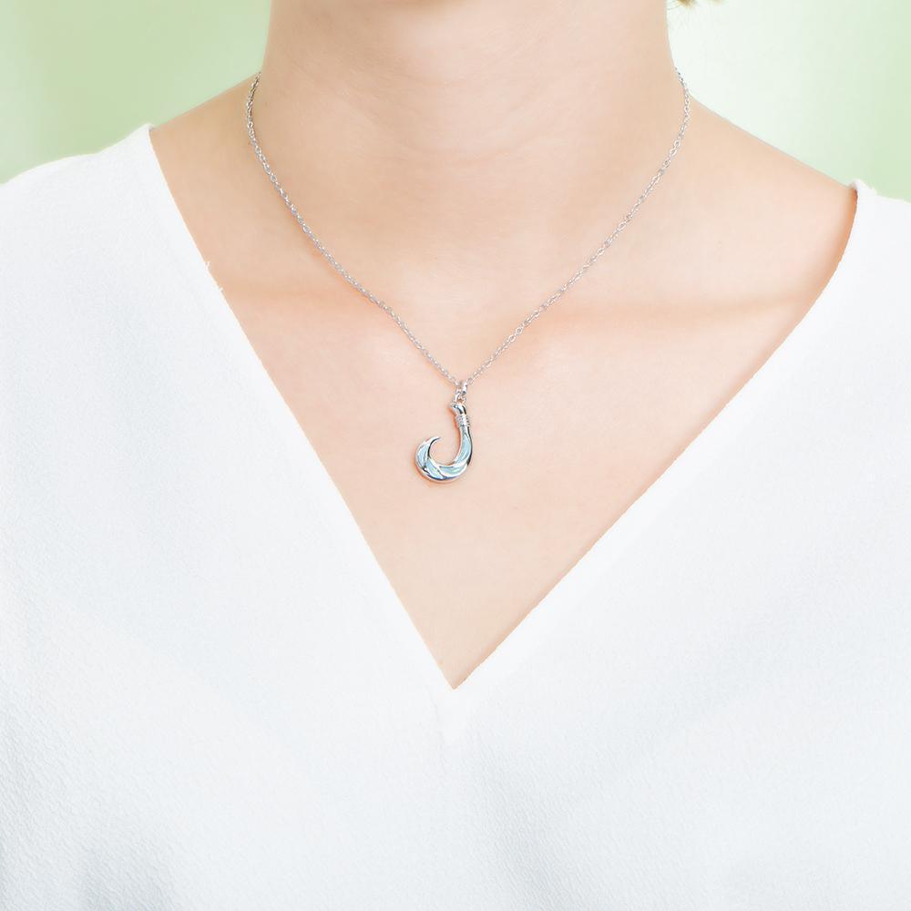 In this photo there is a model with a white shirt wearing a sterling silver fish hook pendant with blue larimar gemstones.