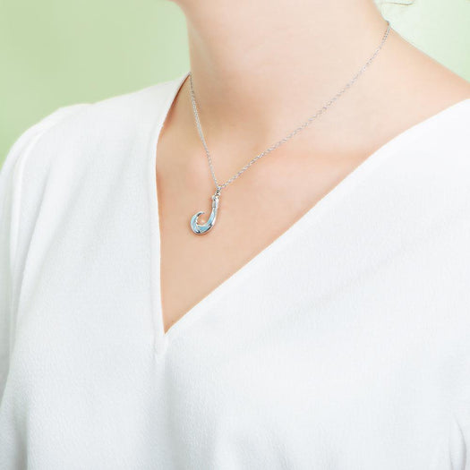 In this photo there is a model with a white shirt turned to the left, wearing a sterling silver fish hook pendant with blue larimar gemstones.