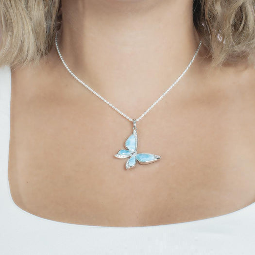 In this photo there is a model with blonde hair and a white shirt, wearing a sterling silver butterfly pendant with blue larimar gemstones and topaz.