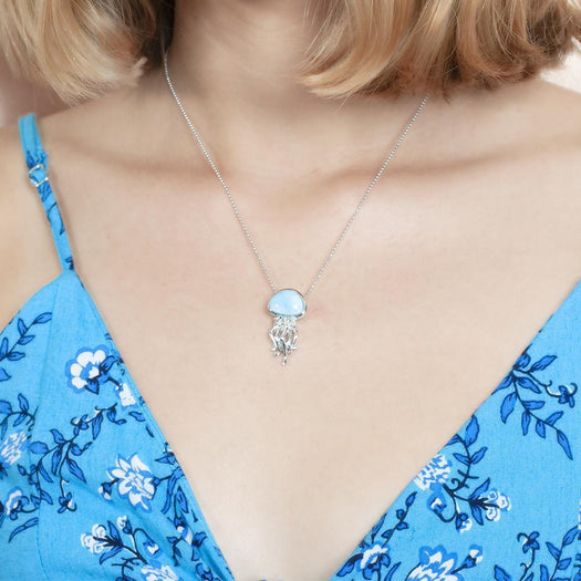 The picture shows a model wearing a 925 sterling silver larimar jellyfish pendant and blue dress with flowers.