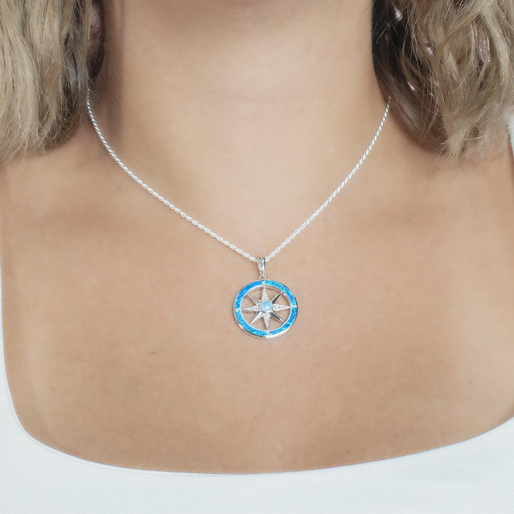 In this photo there is a model with blonde hair and a white shirt, wearing a sterling silver compass pendant with blue larimar, blue opalite, and topaz gemstones.