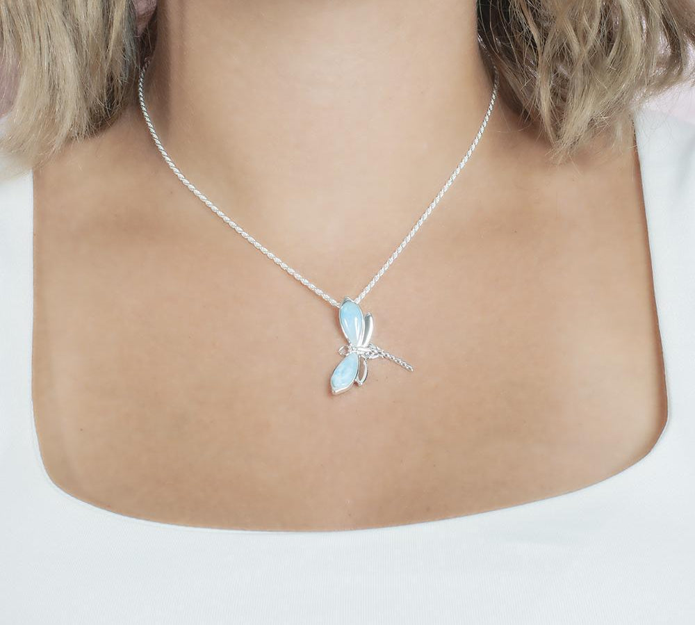 In this photo there is a model with blonde hair and a white shirt, wearing a sterling silver dragonfly pendant with blue larimar gemstones.