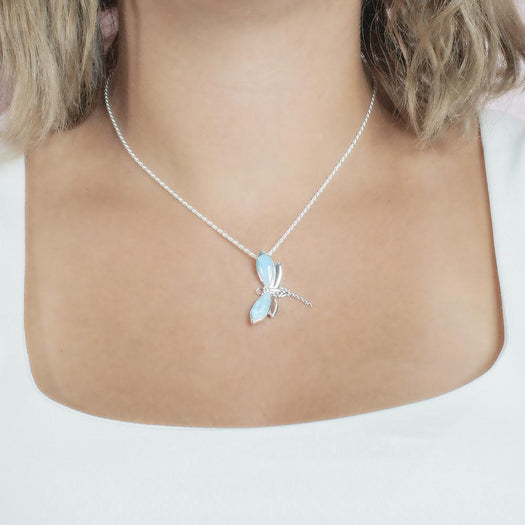 In this photo there is a model with blonde hair and a white shirt, wearing a sterling silver dragonfly pendant with blue larimar gemstones.