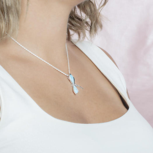 In this photo there is a model turned to the right with blonde hair and a white shirt, wearing a sterling silver dragonfly pendant with blue larimar gemstones.