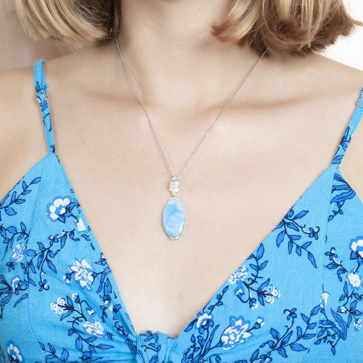 The picture shows a model wearing a 925 sterling silver larimar pendant with topaz and cubic zirconia.