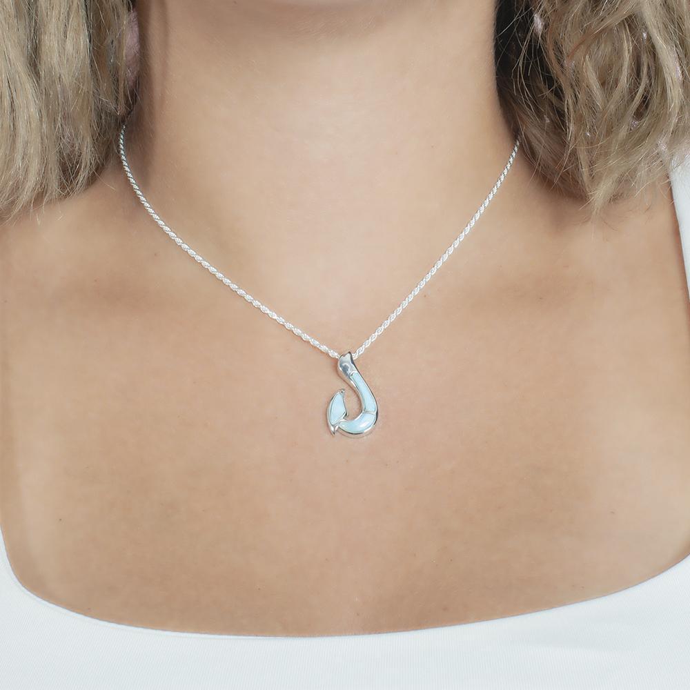 In this photo there is a model with blonde hair and a white shirt, wearing a sterling silver fish hook pendant with blue larimar gemstones.