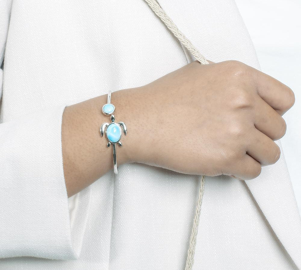 The picture shows a model wearing a 925 sterling silver sea turtle bangle bracelet with two larimar gemstones.