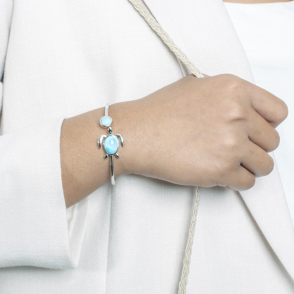 The picture shows a model wearing a 925 sterling silver sea turtle bangle bracelet with two larimar gemstones.