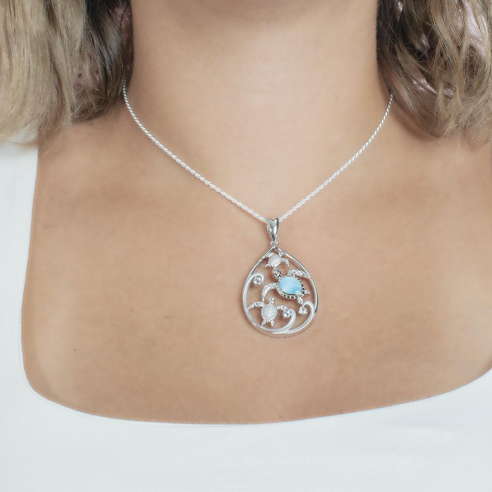 The picture shows a model wearing a 925 sterling silver teardrop shaped pendant with 3 sea turtles in the center with cubic zirconia and larimar.