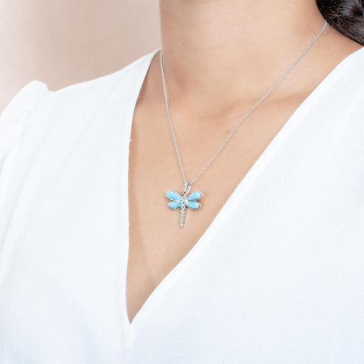 In this photo there is a model with brown hair and a white shirt turned to the left, wearing a sterling silver dragonfly pendant with blue larimar and aquamarine gemstones.