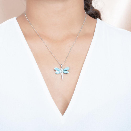 In this photo there is a model with brown hair and a white shirt, wearing a sterling silver dragonfly pendant with blue larimar and aquamarine gemstones.