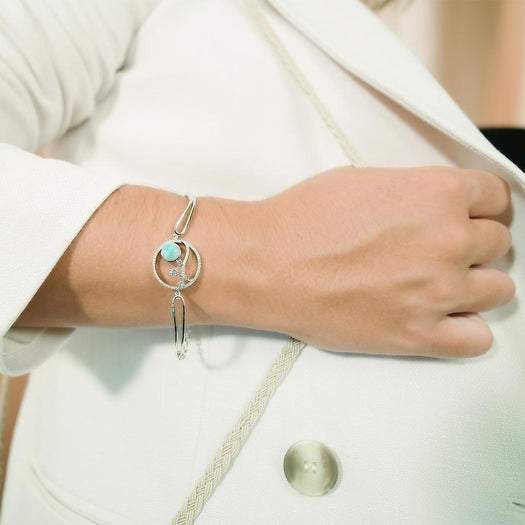 In this photo there is a model wearing a 925 sterling silver bracelet with a wave and sun design with larimar, topaz, and aquamarine gemstones.