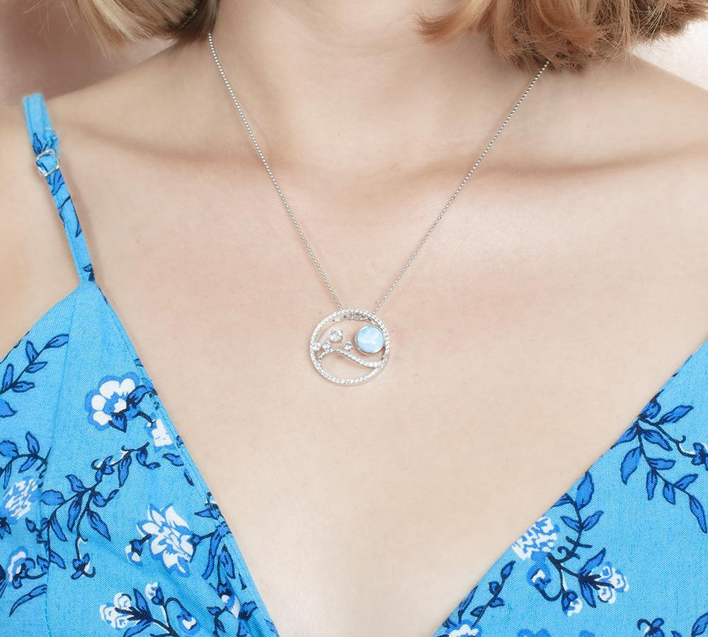 In this photo there is a model with blonde hair and a blue dress with flowers, wearing a sterling silver pendant with blue larimar, aquamarine and topaz.