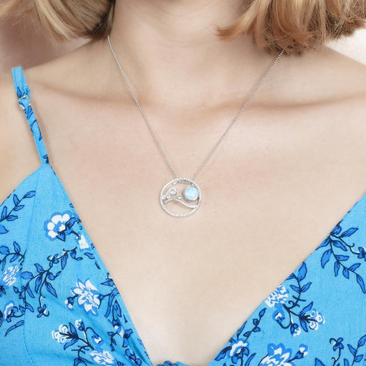 In this photo there is a model with blonde hair and a blue dress with flowers, wearing a sterling silver pendant with blue larimar, aquamarine and topaz.