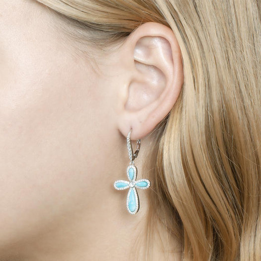 The picture shows a model wearing a 925 sterling silver larimar cross lever-back earring with topaz.