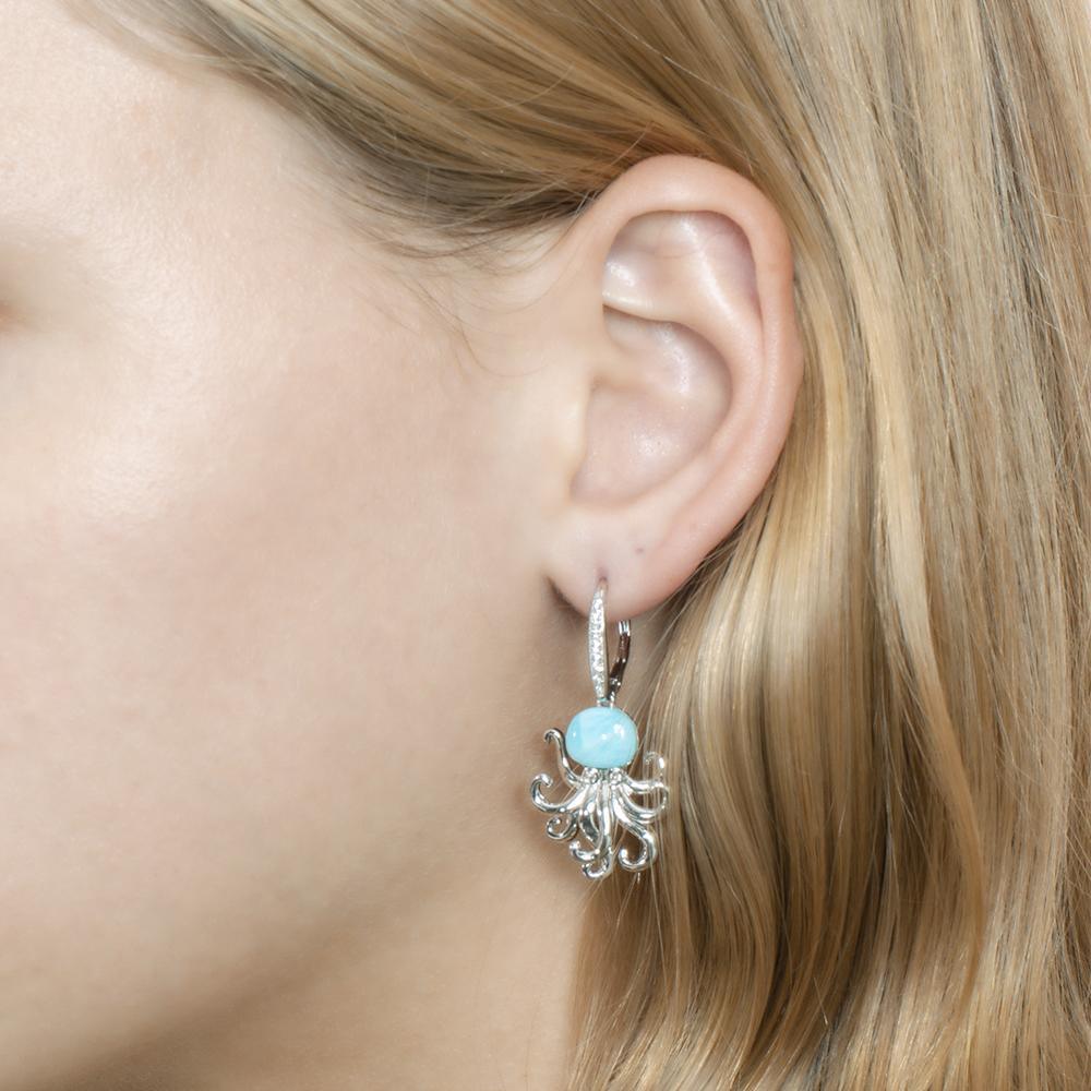 The picture shows a model wearing a 925 sterling silver larimar octopus lever-back earring with topaz and aquamarine gemstones.