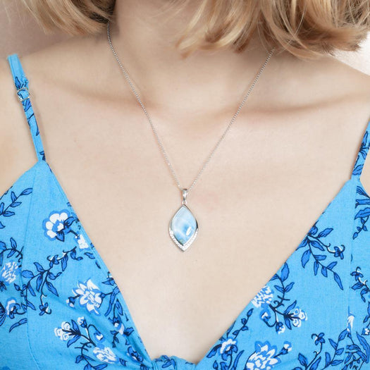 The picture shows a model wearing a blue dress and a 925 sterling silver larimar loa mandorla pendant with topaz.