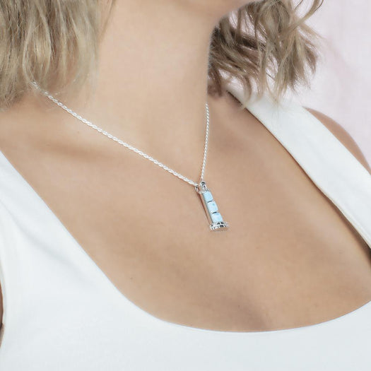 In this picture there is a model with blonde hair and a white shirt turned to the right wearing a lighthouse pendant with blue larimar gemstones set in sterling silver.