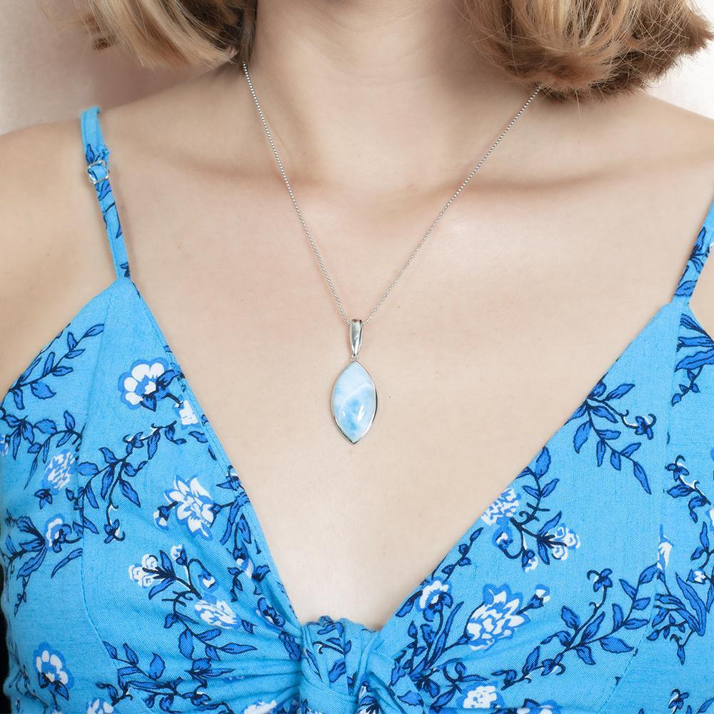 The picture shows a model wearing a 925 sterling silver larimar mandorla pendant and a blue dress with flowers.