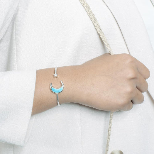 The picture shows a model wearing a 925 sterling silver larimar moon and star sleek bangle with topaz.