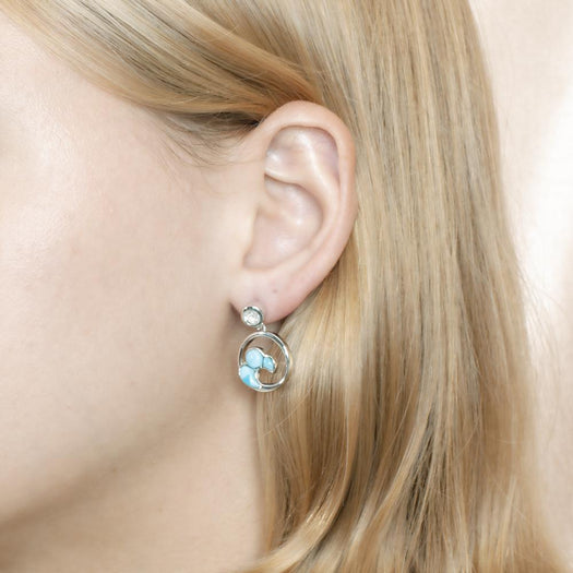 The picture shows a model wearing a 925 sterling silver larimar wave earring with topaz