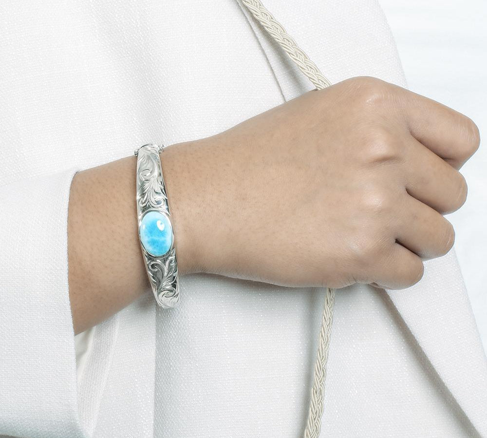 The picture shows a model wearing a 925 sterling silver bangle with one oval larimar gemstone and engravings.