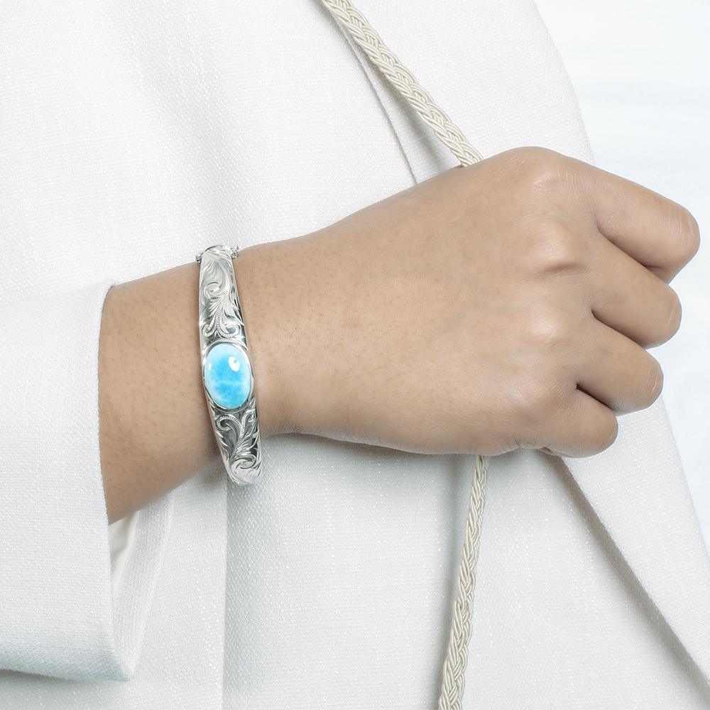The picture shows a model wearing a 925 sterling silver bangle with one oval larimar gemstone and engravings.