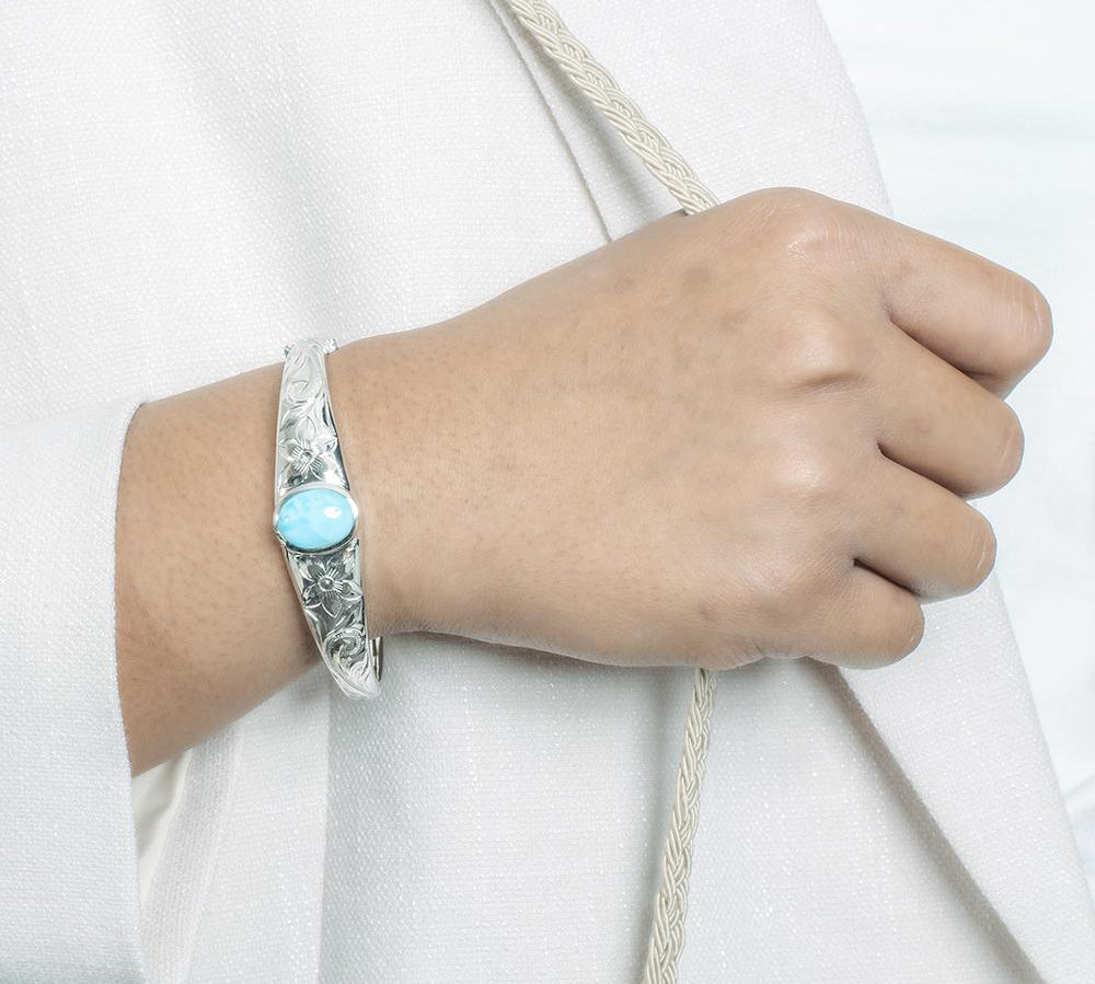 In this photo there is a model wearing a 925 sterling silver bangle with one blue larimar gemstone and plumeria engravings.